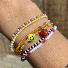 Load image into Gallery viewer, multi colored, patterned seed bead bracelet with a yellow smiley face bead, yellow red striped beaded bracelet with enamel strawberry charm
