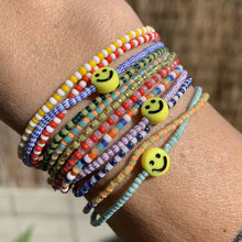 Load image into Gallery viewer, multi colored red, blue, green, white striped seed bead bracelet with a yellow smiley face bead
